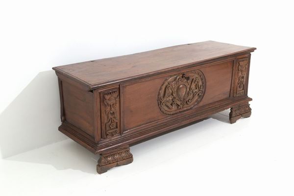 Cassapanca in legno di noce scolpito e intagliato con fregio e mascheroni. Fiul...