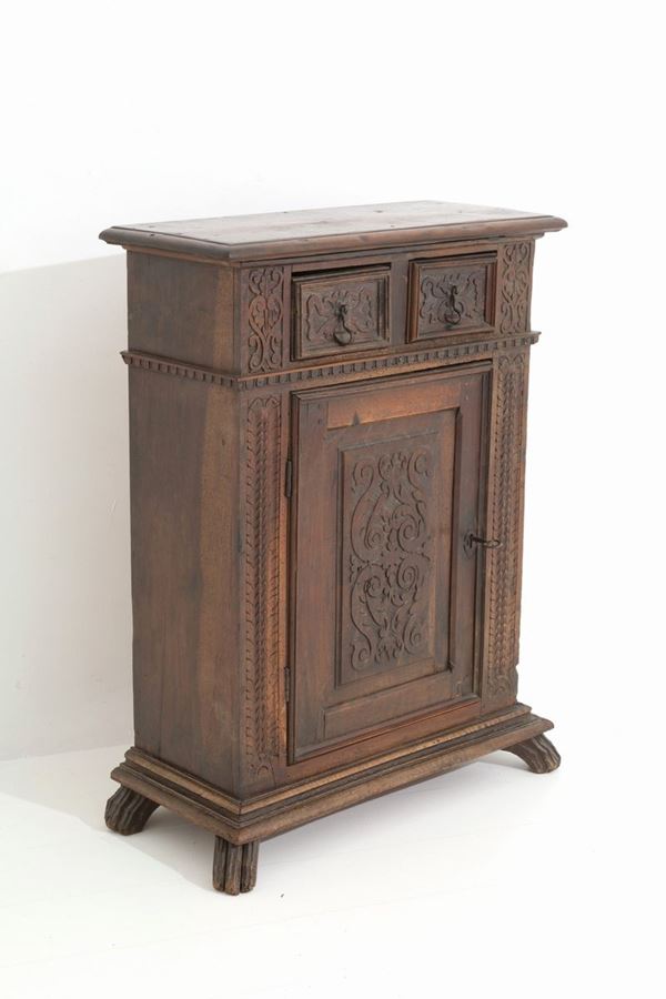Credenzina in legno di noce intagliato con un'anta e due cassetti. Italia del N...